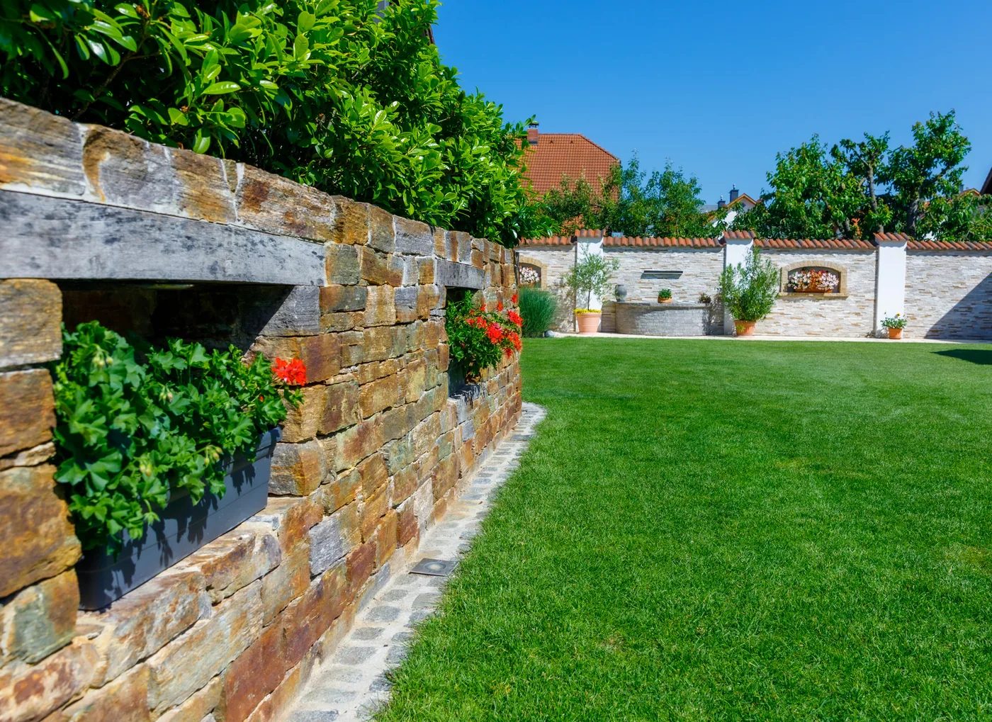 Geschnittene Hecke auf einer niedrigen Mauer vor dem verglasten Anbau