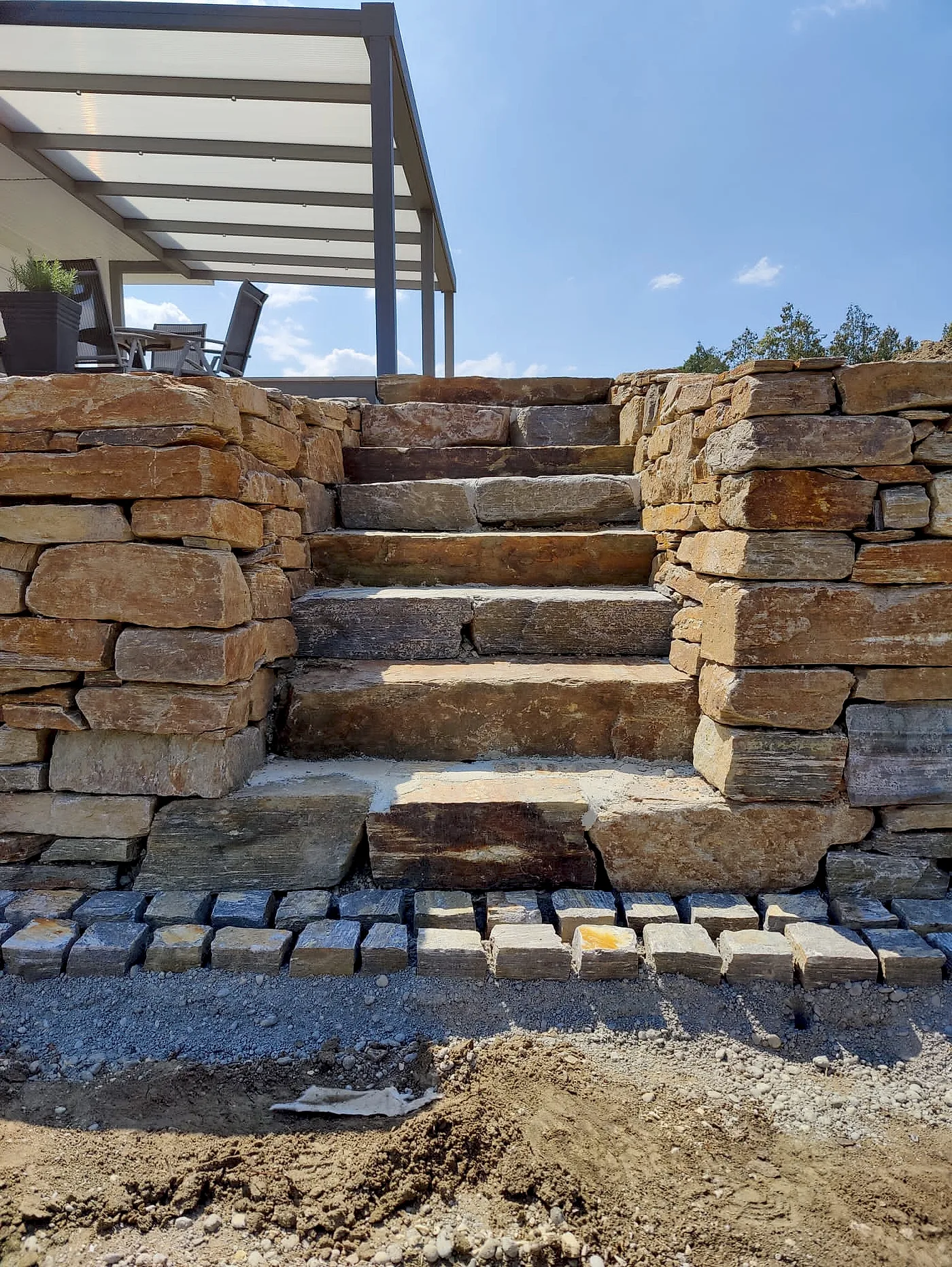 Sitzbereich vor einer hellen Natursteinmauer mit Blockstufen