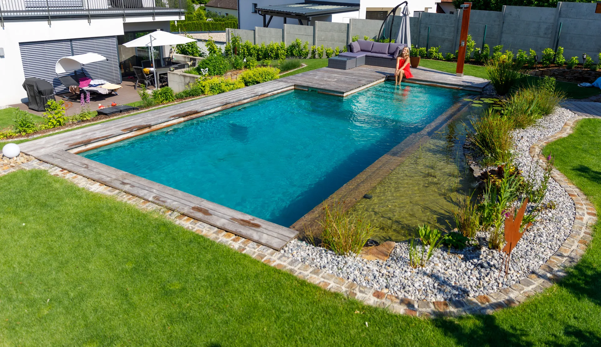 Fertiger Schwimmteich mit Holzdeck und Kiesufer im Familiengarten