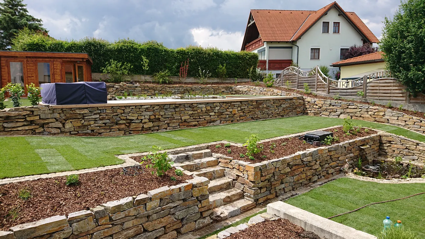 Terrassierter Garten mit Natursteinmauern und frischem Rasen