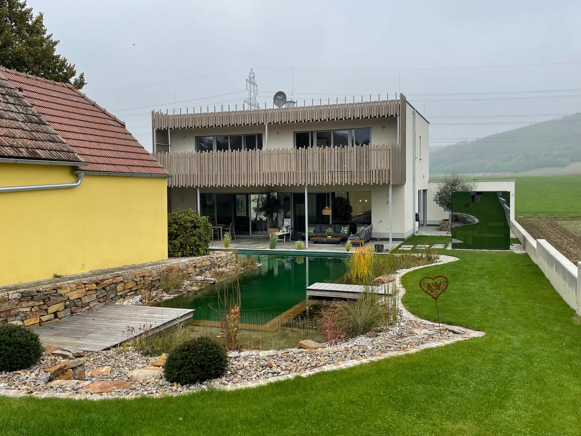 Fertiger Schwimmteich mit Natursteinmauer und Rasen am modernen Haus
