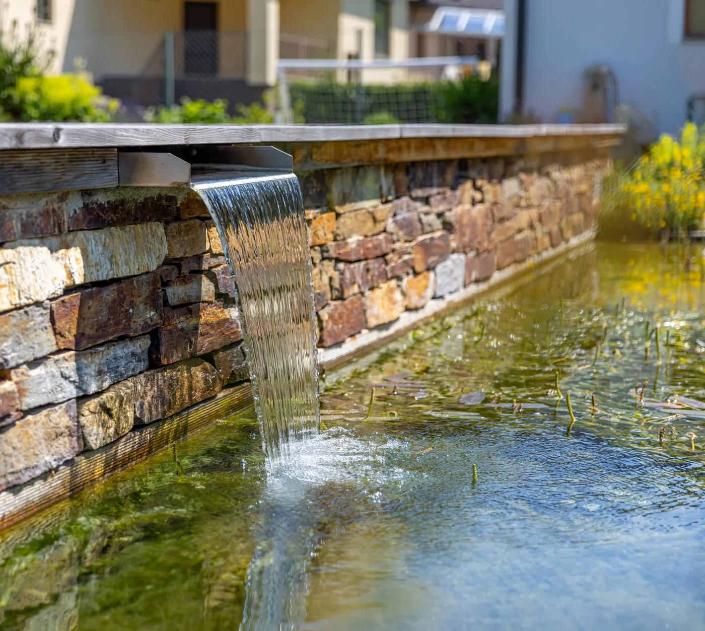 Wasserfall fließt über die Natursteinmauer des Naturpools