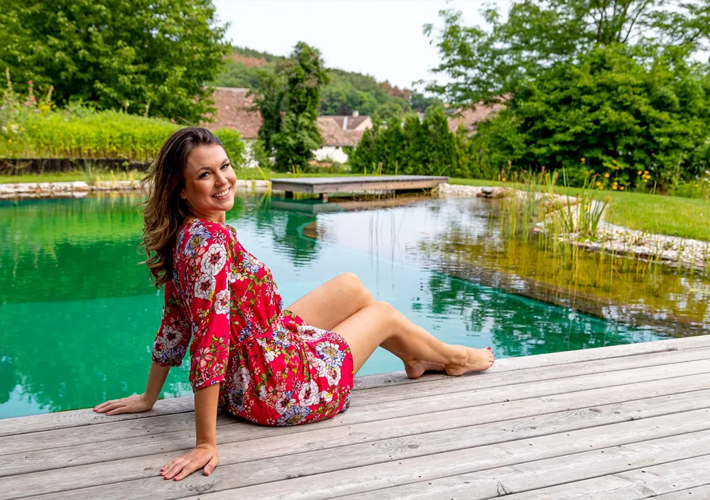 http://Frau%20sitzt%20auf%20dem%20Holzdeck%20eines%20Naturpools