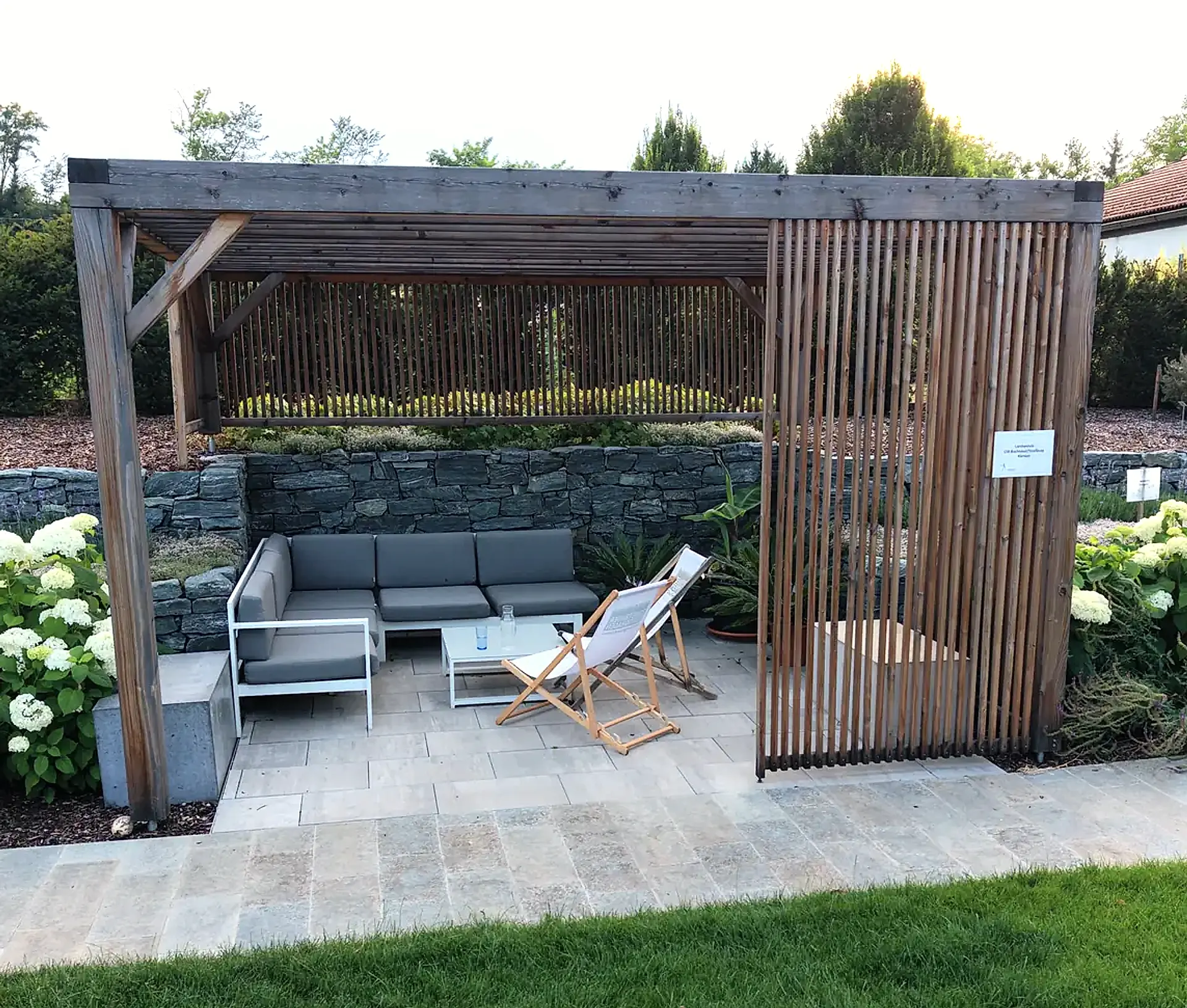 Pergola aus Holz mit Loungemöbeln und Sichtschutzlamellen auf einer Plattenterrasse