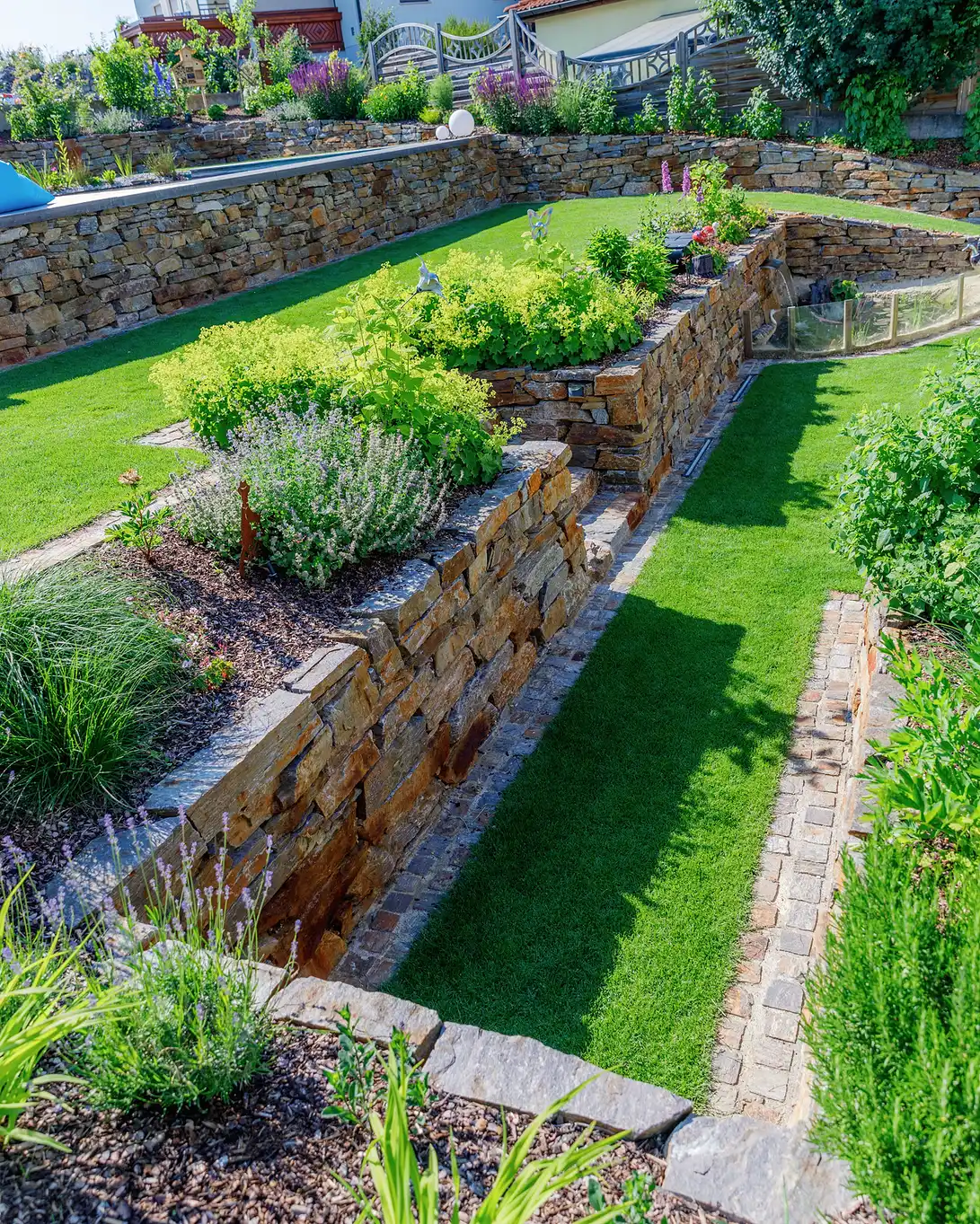 Mehrstufig terrassierte Beete mit Sandsteinmauern und Rasenweg dazwischen