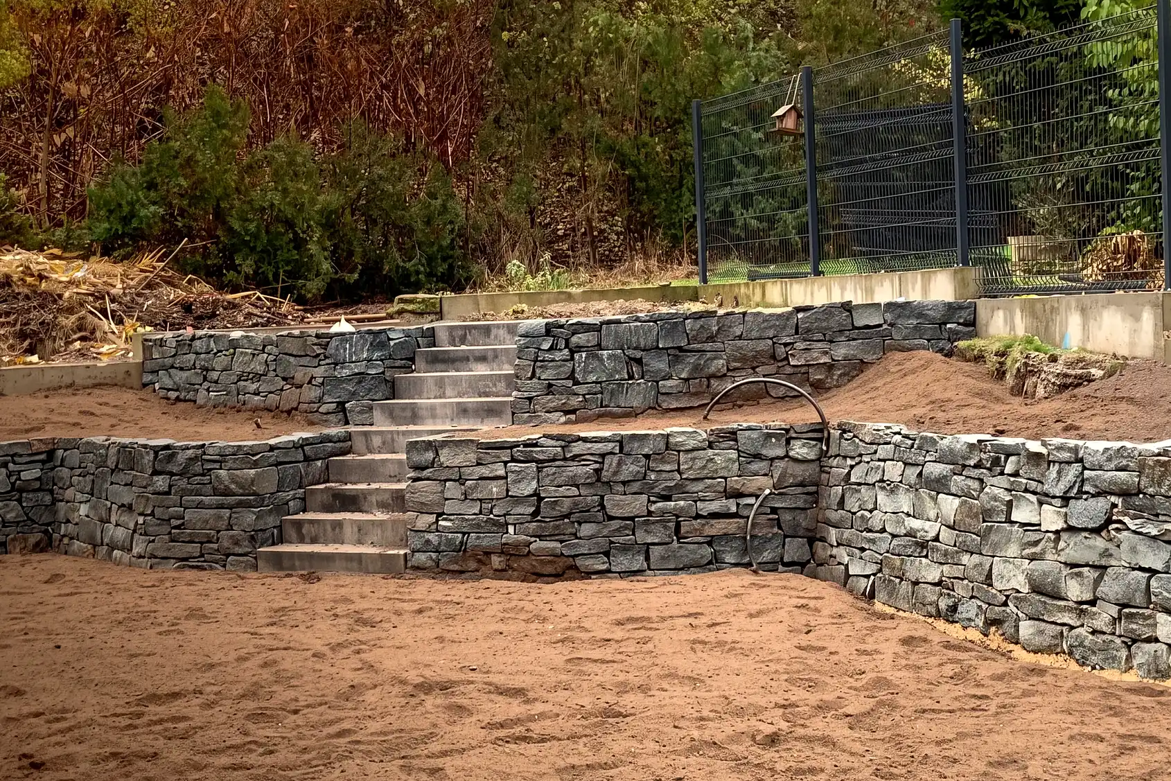 Geschichtete Natursteinstufen treffen auf die Wange einer Trockenmauer