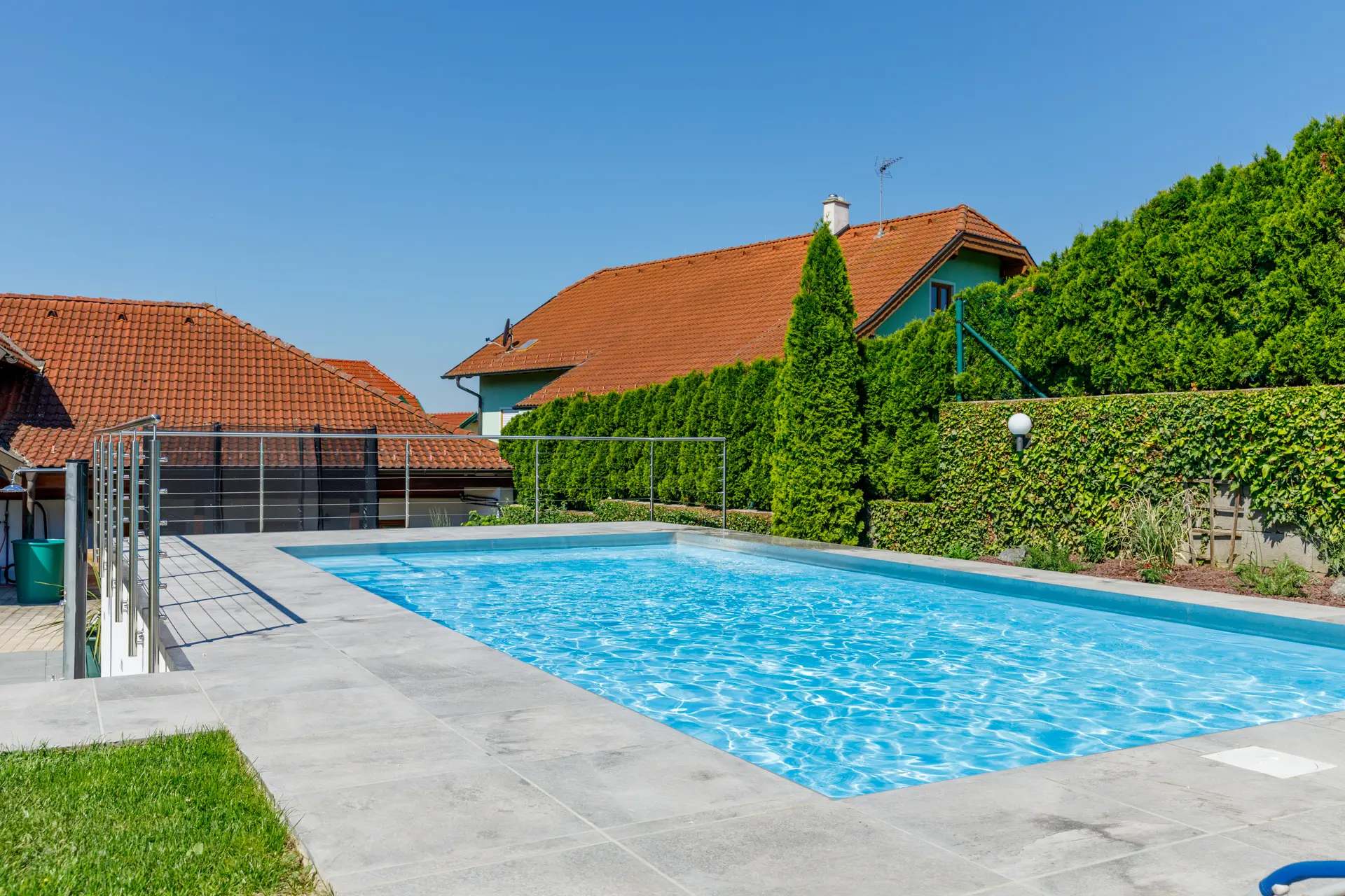 Rechteckiger Pool mit blauem Wasser und heller Plattenterrasse ringsum