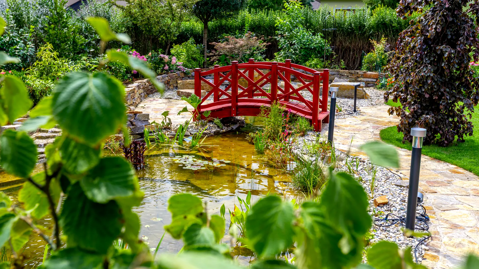 Naturpool mit Sonnenschirm, Gartenhaus und blühenden Beeten
