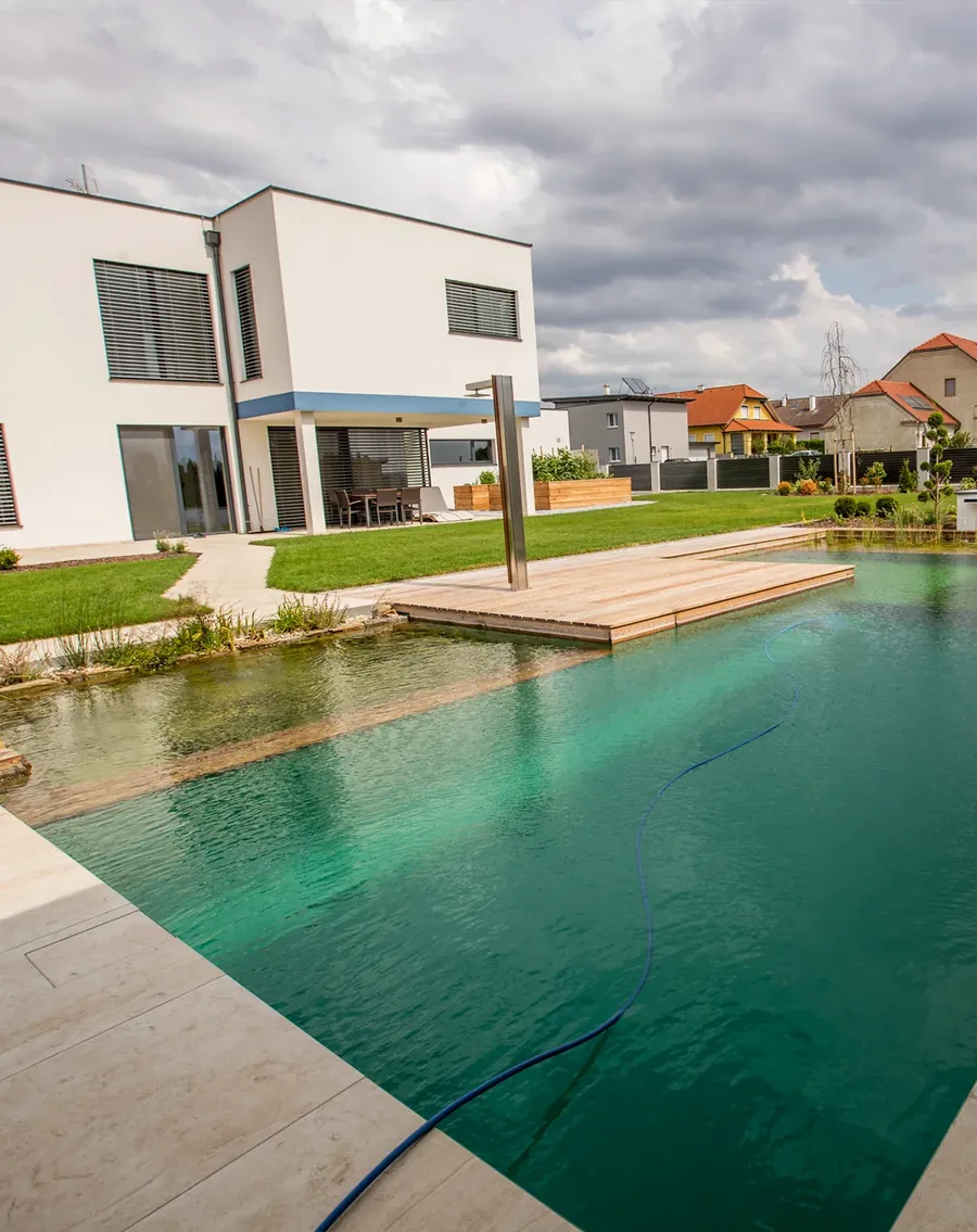 Naturpool mit Holzdeck vor einem modernen Wohnhaus