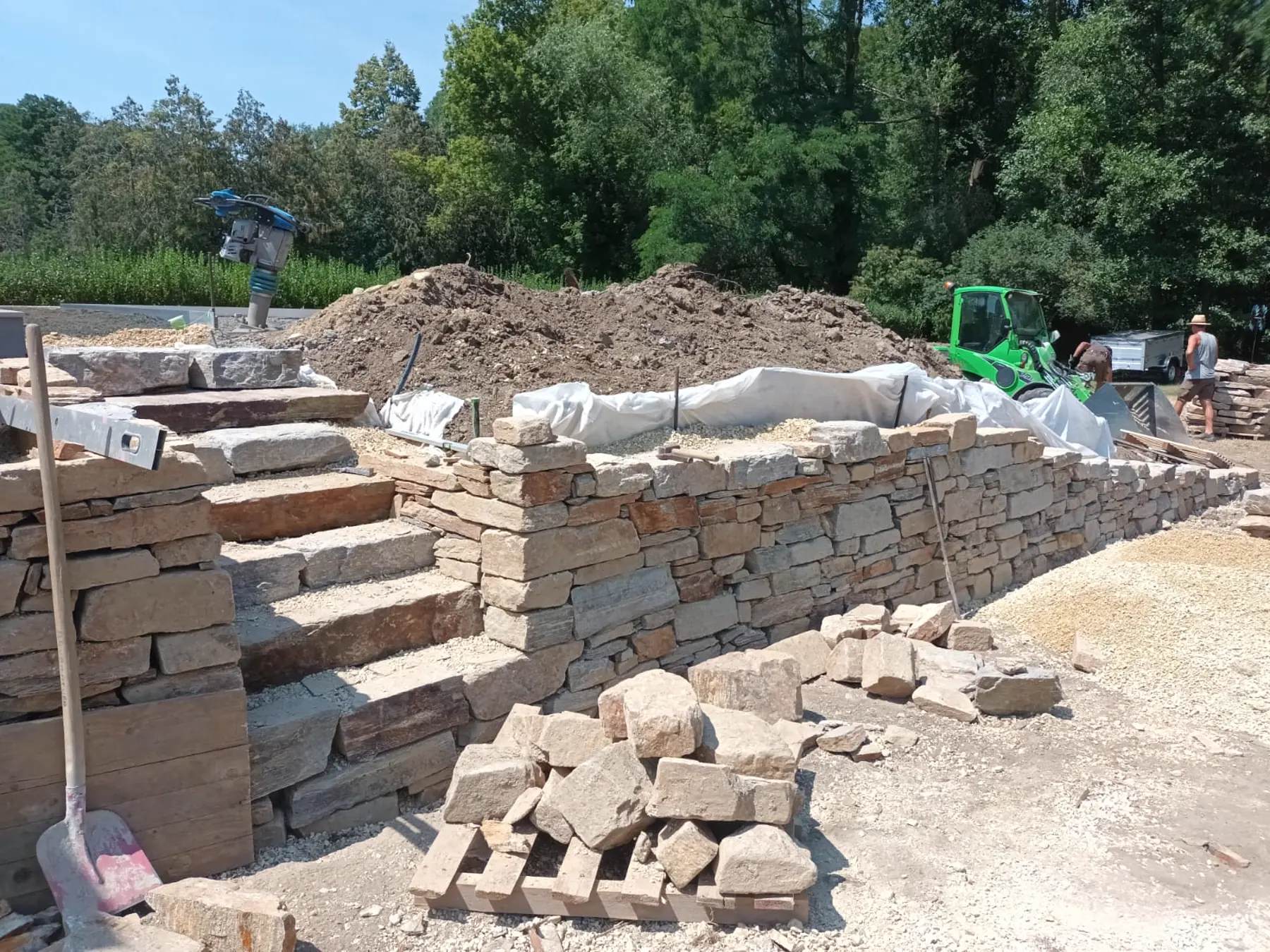 Baustelle mit lagenweise verdichtetem Unterbau und angelieferten Natursteinen
