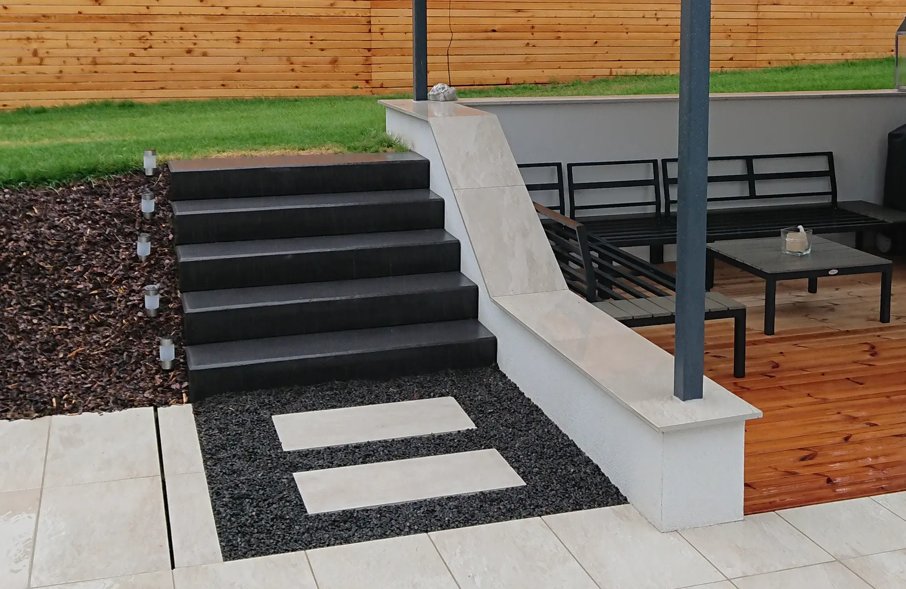 Dunkle Betontreppe mit heller Wange und Trittplatten im Kies