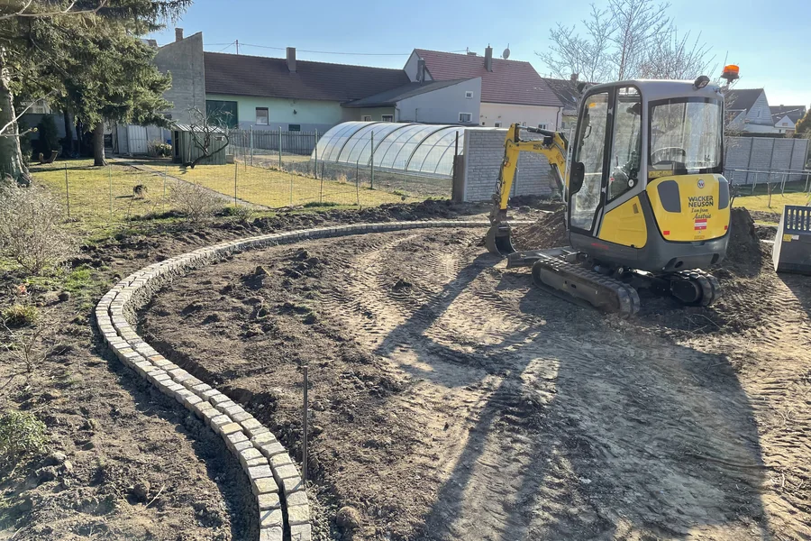 Gesetzte Randsteine entlang eines geschwungenen Weges, dahinter der Minibagger beim Planum