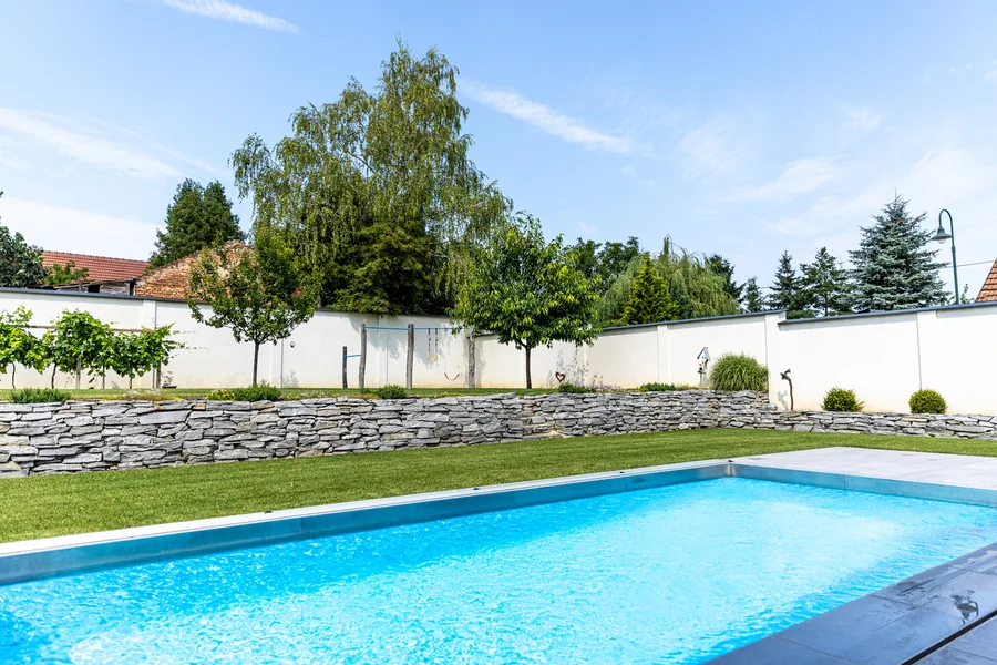 Rechteckiger Pool mit türkisem Wasser vor einer Natursteinmauer und geschnittener Hecke