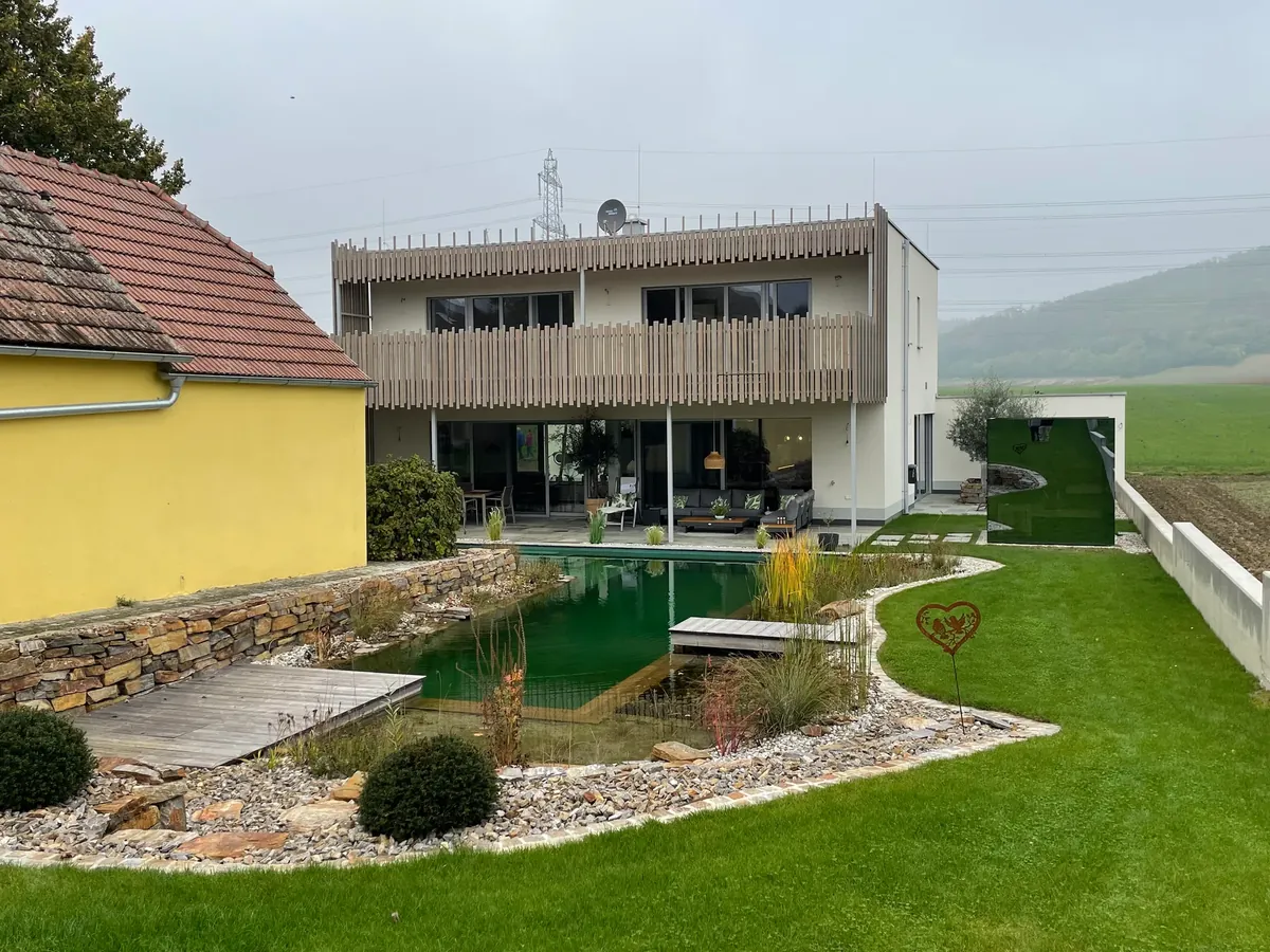 Schwimmteich vor einem Wohnhaus mit Natursteinmauer