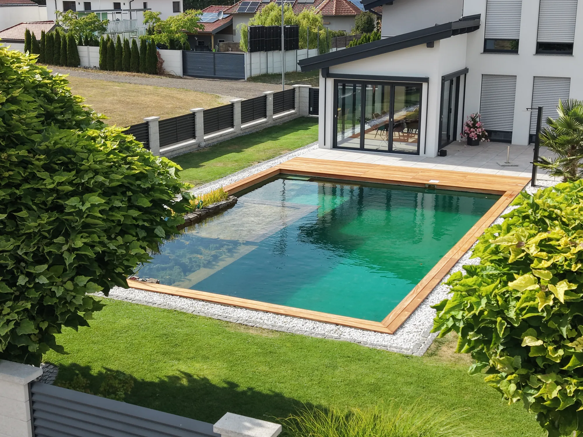 Schwimmteich mit Sträuchern und Rasen neben dem Haus
