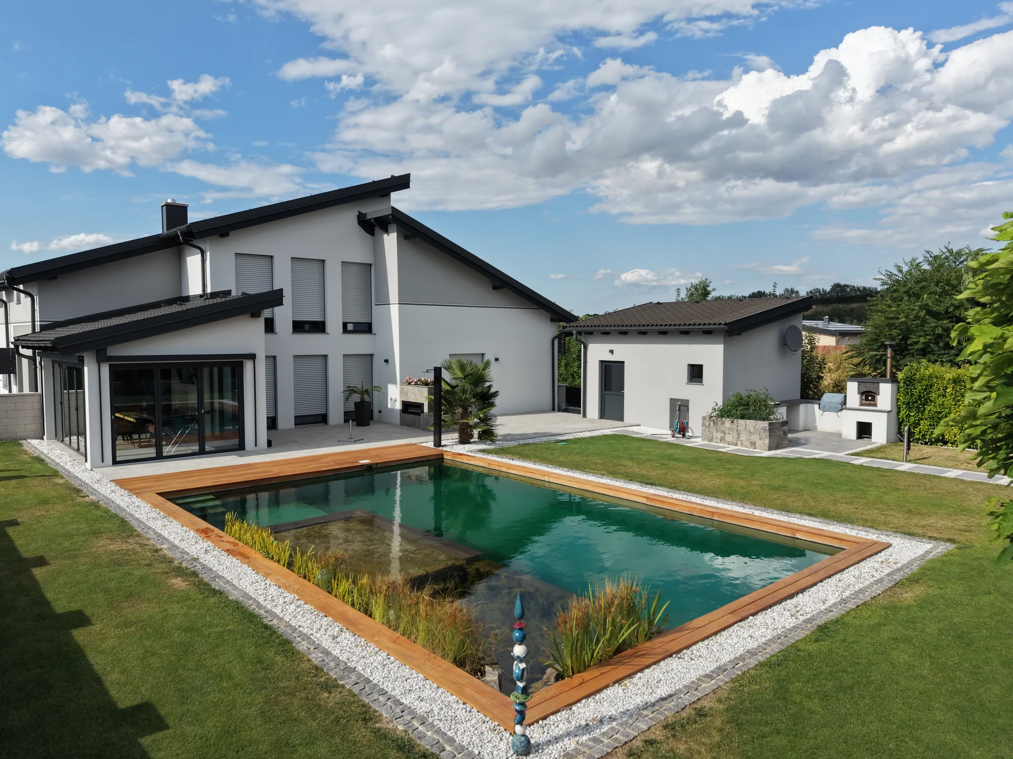 Rechteckiger Schwimmteich mit breitem Holzdeck vor einem modernen Haus