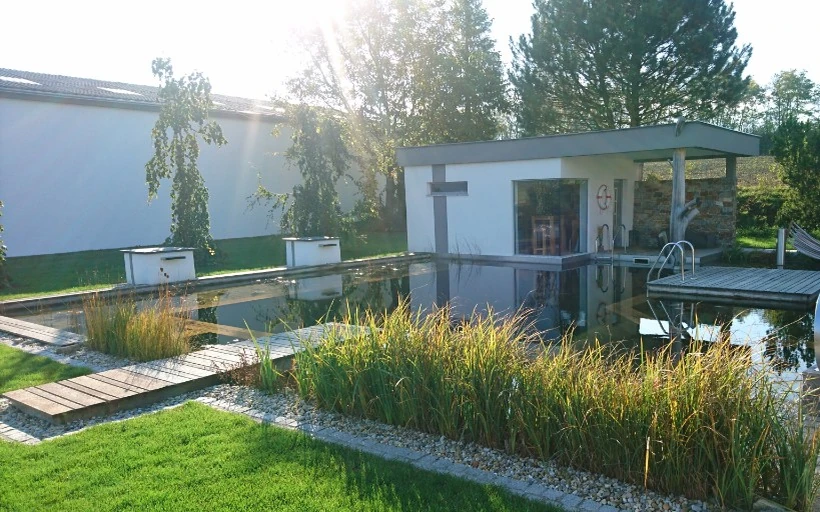 Schwimmteich der Schauanlage mit bepflanztem Ufer und angrenzender Rasenfläche