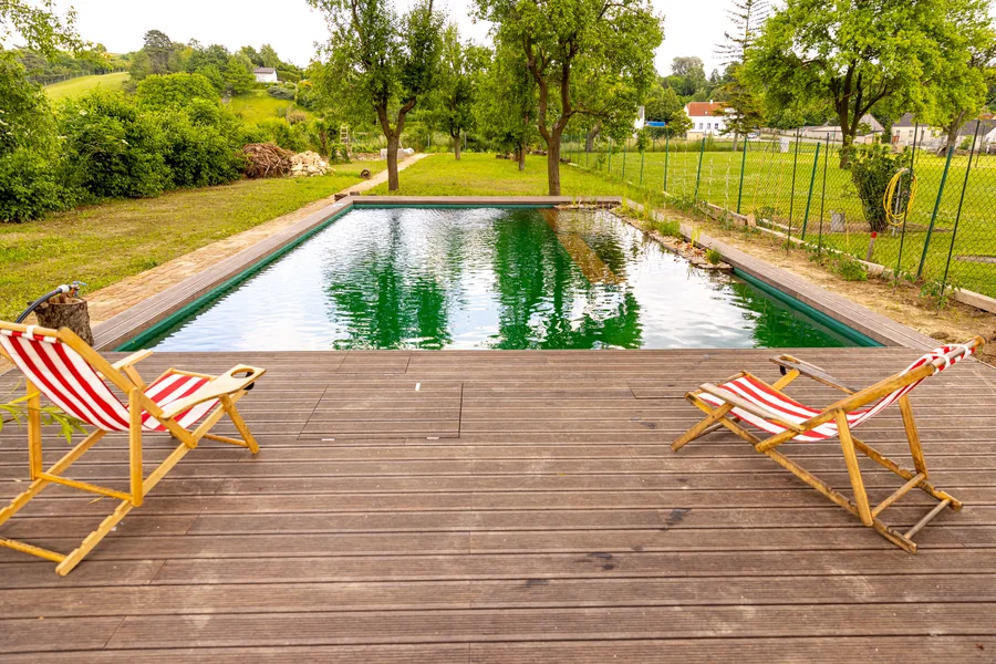 Breites Holzdeck mit Liegestühlen am Rand eines Naturpools