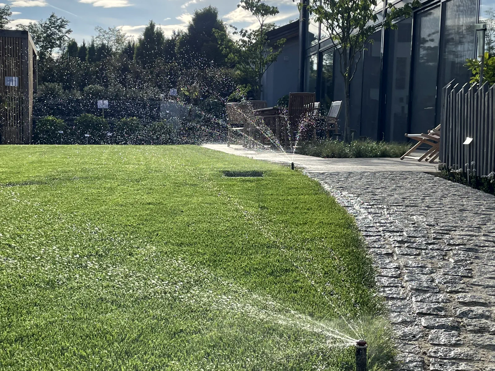 Versenkregner bewässern den Rasen vor einer Glasfassade