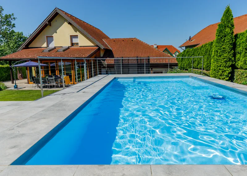 Klassischer Pool mit heller Terrassenfläche vor einem Wohnhaus